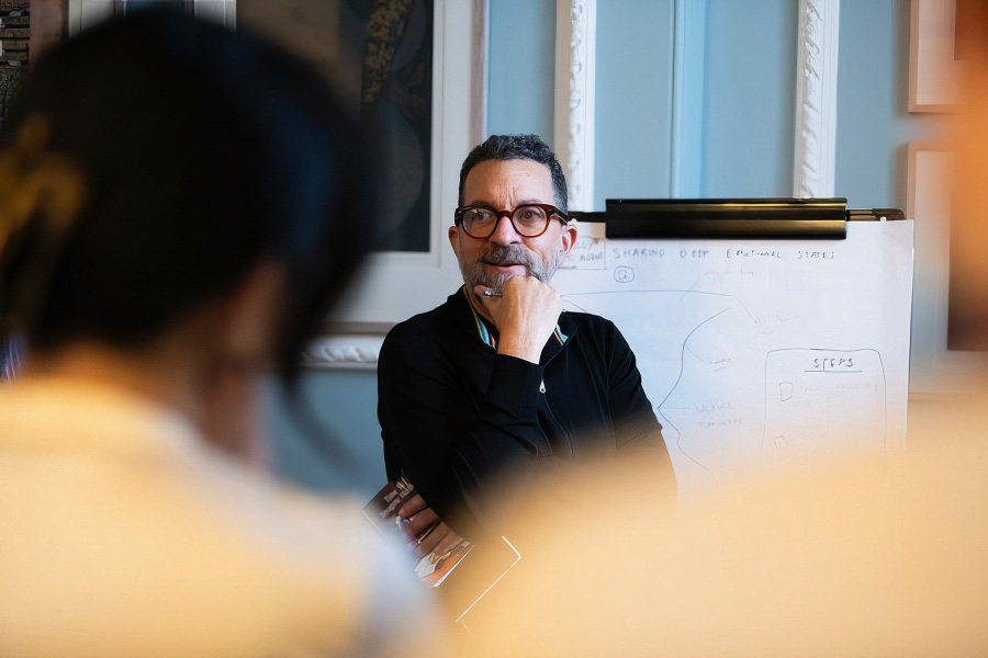 A portrait of Dr. Julian Bleecker during a workshop looking towards a participant who is in the foreground with heavy bokeh.